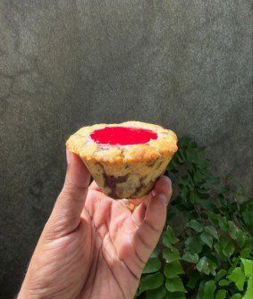 A small cookie tartlet with a glossy red centre, held between finger and thumb.