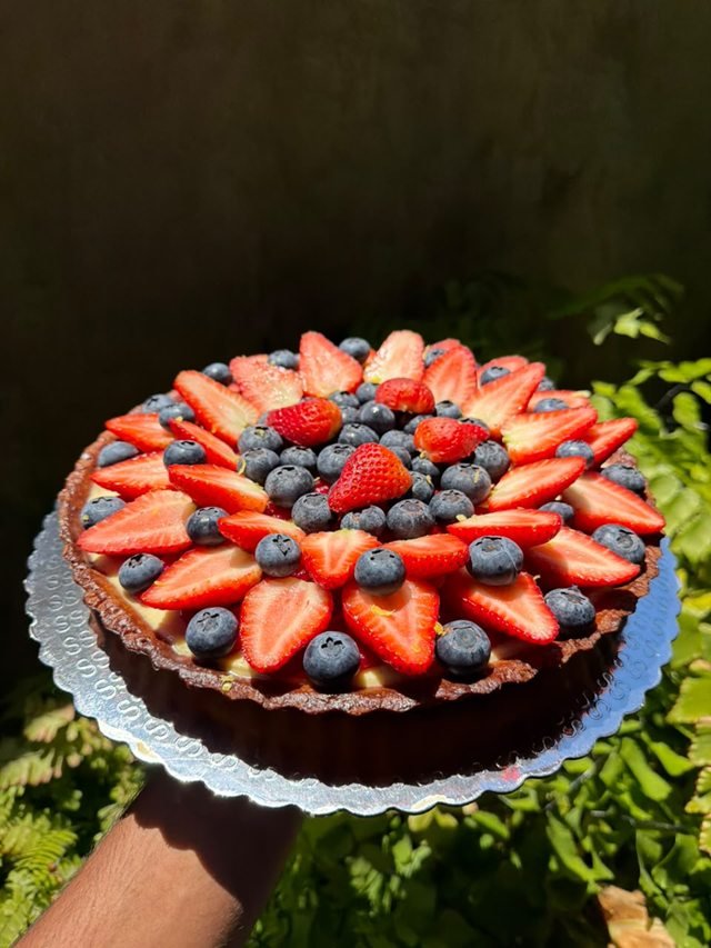 A fruit tart heaped with halved strawberries and blueberries in a dark fluted pastry shell.