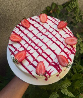 A round cake finished with white cream, a berry drizzle lattice and halved strawberries.