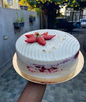A smooth white cake finished with a flower of sliced strawberries at its centre.